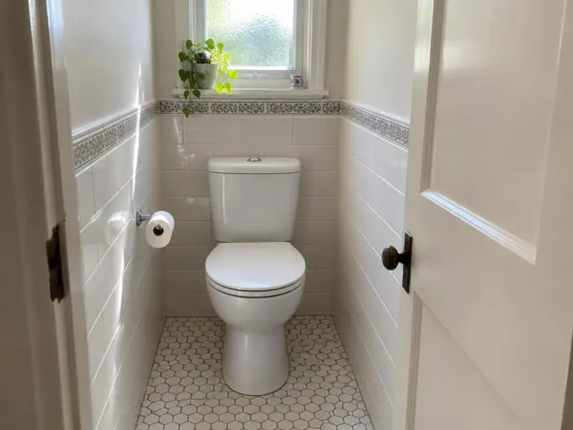 Clean white toilet in a small tiled bathroom with hex floor tiles and a window in Roseville
