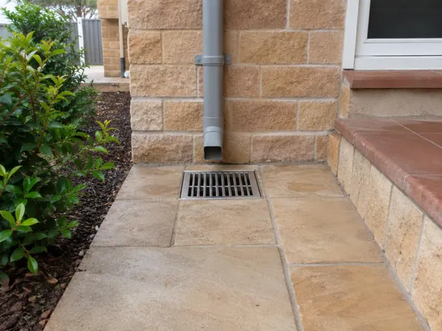 Outdoor paved gully grate beside a brick wall and downpipe, with dry paving in Lindfield