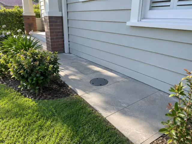 Capped round access point in reinstated paving beside a weatherboard house in Chatswood